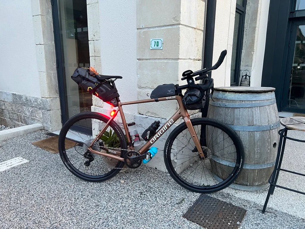 Un vélo gravel équipé en bikepacking (sacoche de selle, sacoche de cadre et sacoche de guidon), posé contre un mur.